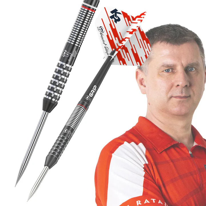 Angled close-up of 90% tungsten darts showing detailed grip pattern, black barrels, red and white flights, with player in background