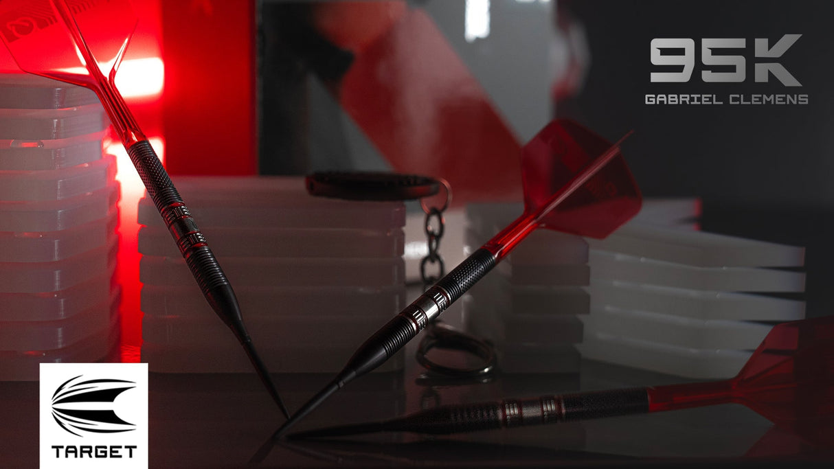 Angled lifestyle shot of two 95% tungsten darts with red flights and knurled grip barrels, displayed among dart cases under red lighting