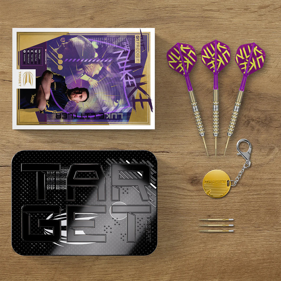 Top-down view of Luke Littler G1 Prodigy darts set with three purple-gold darts, accessories, case, player card, and spare dart points.