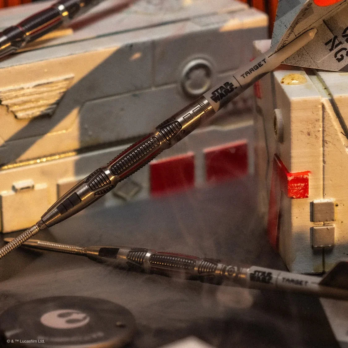 Angled close-up of two 90% tungsten darts with X-Wing flight design and textured grip, displayed on Star Wars decor.