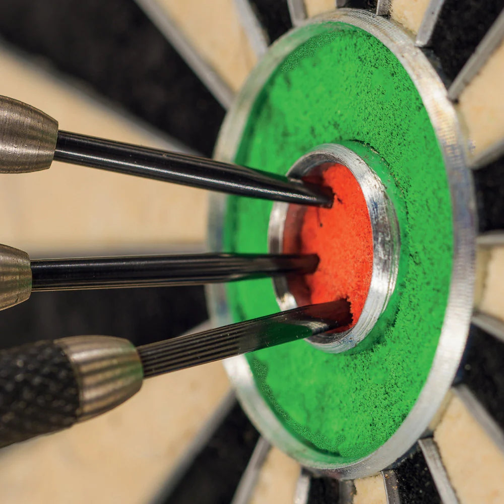 Macro close-up of three steel tip darts grouped tightly in bullseye on bristle dartboard, showing scoring accuracy and fine grip detail