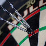angled close-up of three 90% tungsten darts grouped in a dartboard, highlighting detailed barrel grip texture and steel tip design