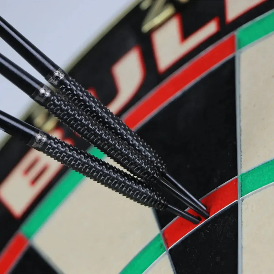 Close-up angled view of three 90% tungsten darts with textured black shark grip barrels grouped on a dartboard's double segment