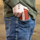 Slim darts case in textured red sliding into jeans pocket, lifestyle view showing compact portable dart storage