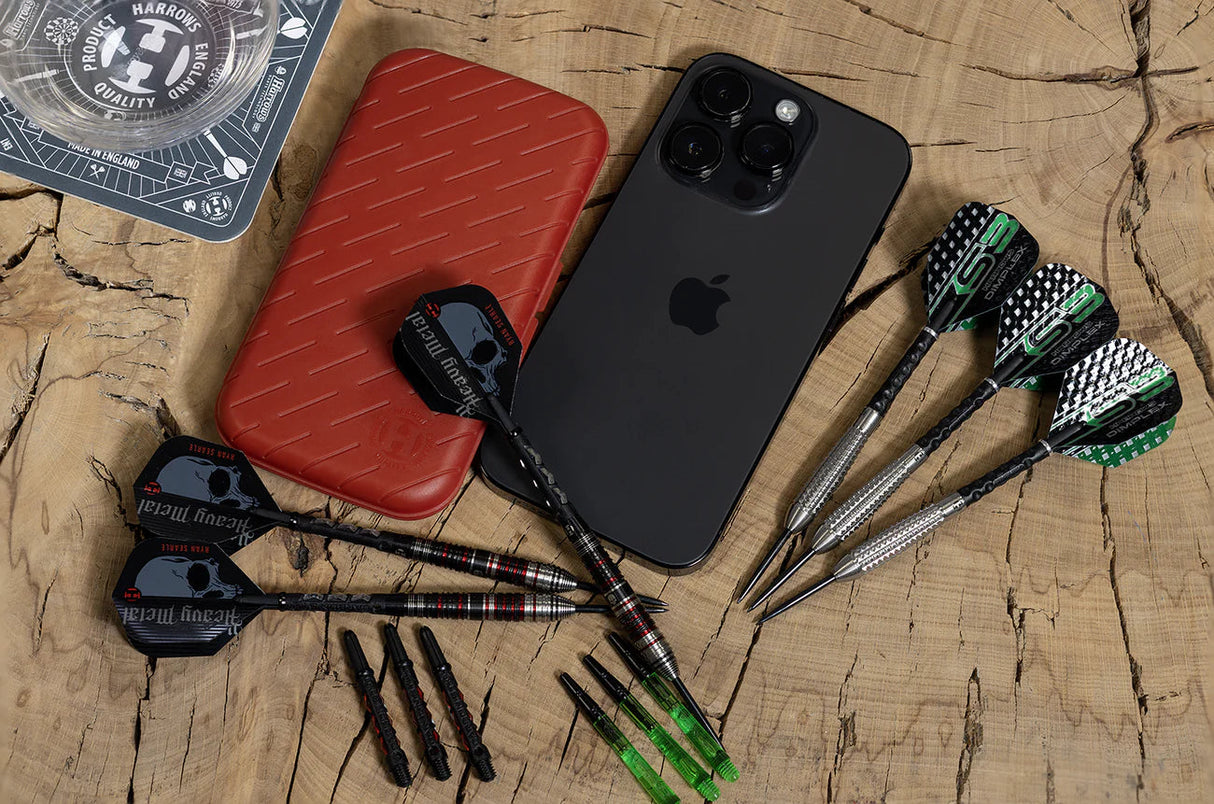 Top-down view of slim darts case beside phone for size, with assembled darts, spare shafts, and flights on wooden background