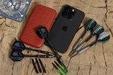 Top-down view of slim darts case beside phone for size, with assembled darts, spare shafts, and flights on wooden background