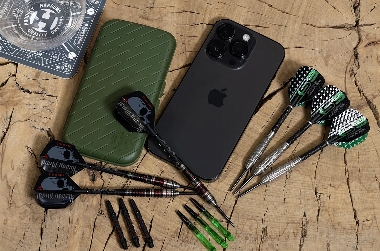 Top-down view of slim darts case next to sets of assembled darts, spare shafts, and smartphone for size comparison on wood background