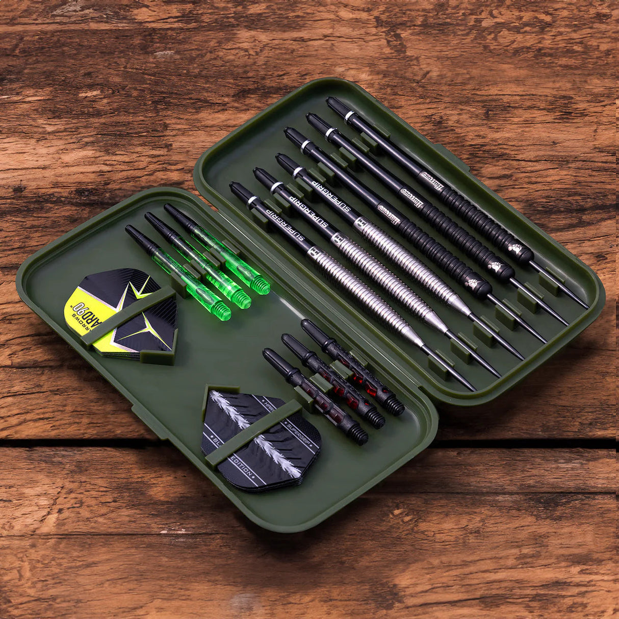 Top-down view of open darts case with six assembled darts, extra shafts, and flights organized on rustic wood background