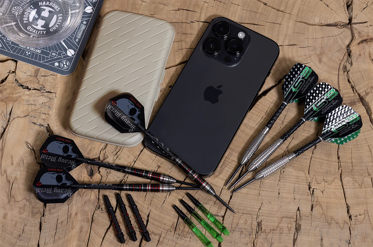 Top-down view of slim darts case beside smartphone, with two sets of darts, spare stems, and flight designs on a wood display