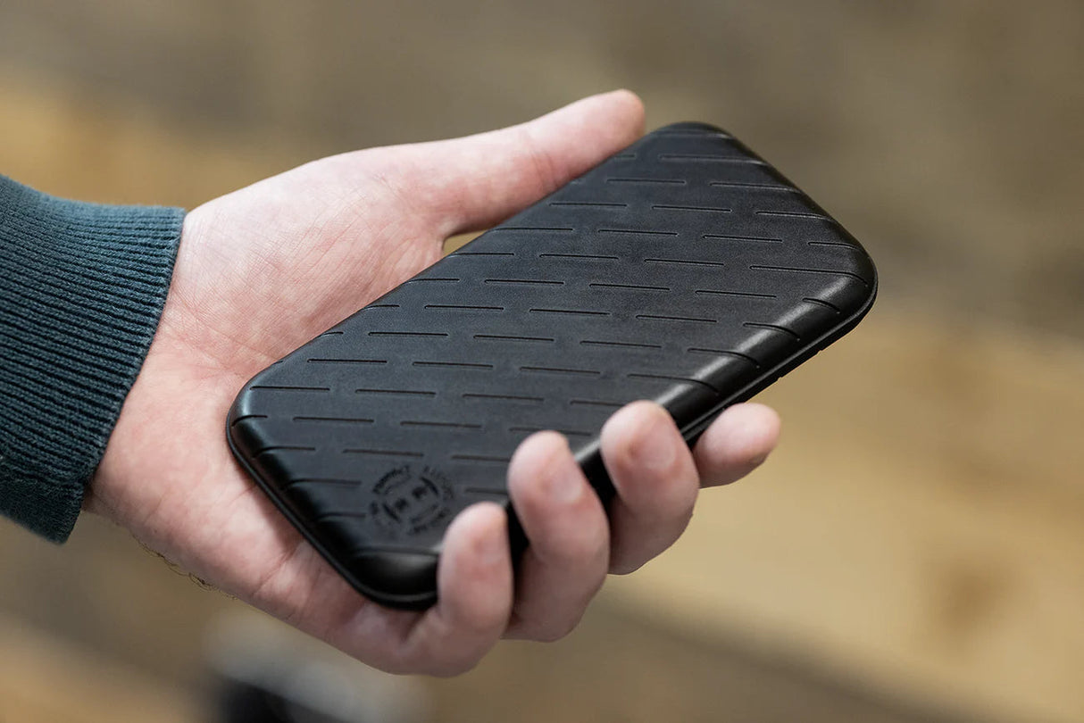 Slim black darts case with textured grip shown in hand for scale, highlighting compact dart storage design