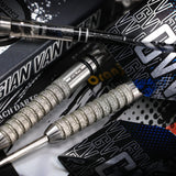 Macro close-up of 90% tungsten darts showing textured grip barrels, black and blue flights, arranged near Gian Van Veen packaging
