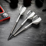 Three 85% tungsten darts with ringed grip barrels and white flights shown angled on black surface, close to packaging for size reference