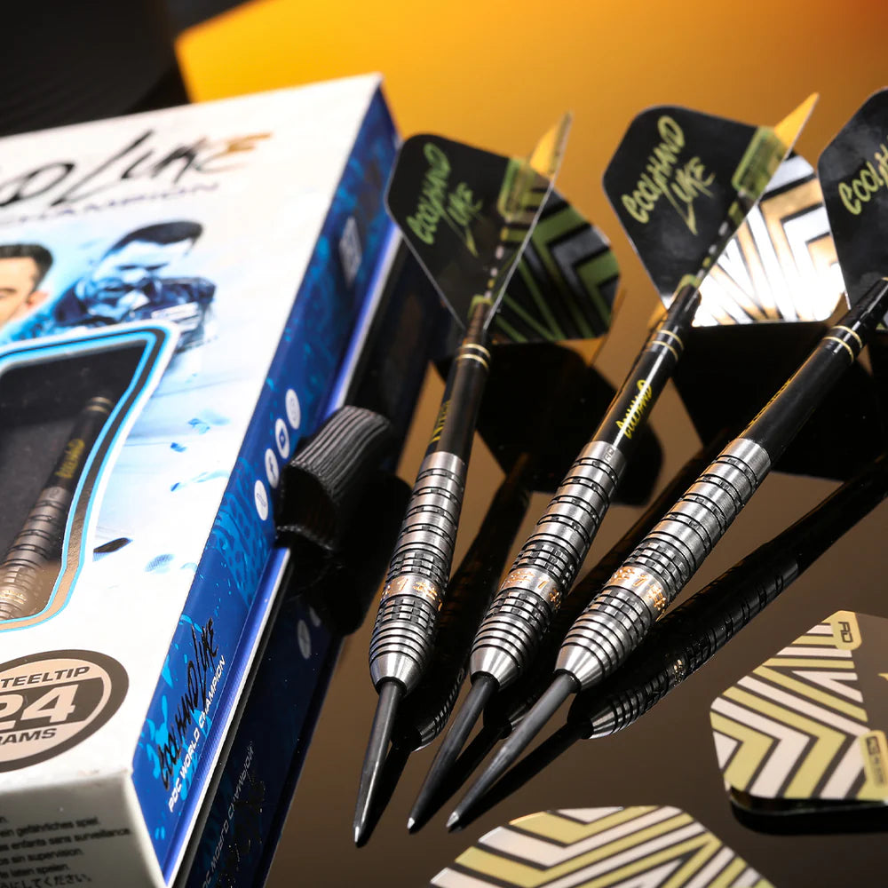 Angled view of three 90% tungsten darts with precision grooved barrels and stylish flights beside retail packaging on reflective surface