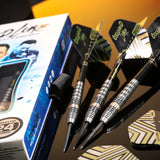 Angled view of three 90% tungsten darts with precision grooved barrels and stylish flights beside retail packaging on reflective surface