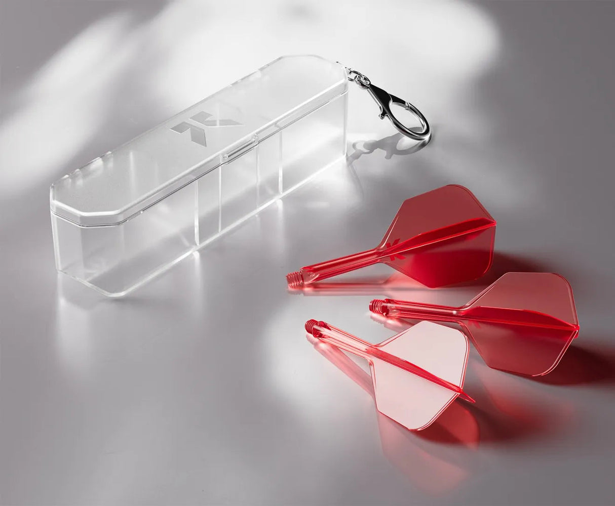 Angled view of transparent hard dart case with keychain, three red dart flights and shafts displayed beside on neutral background