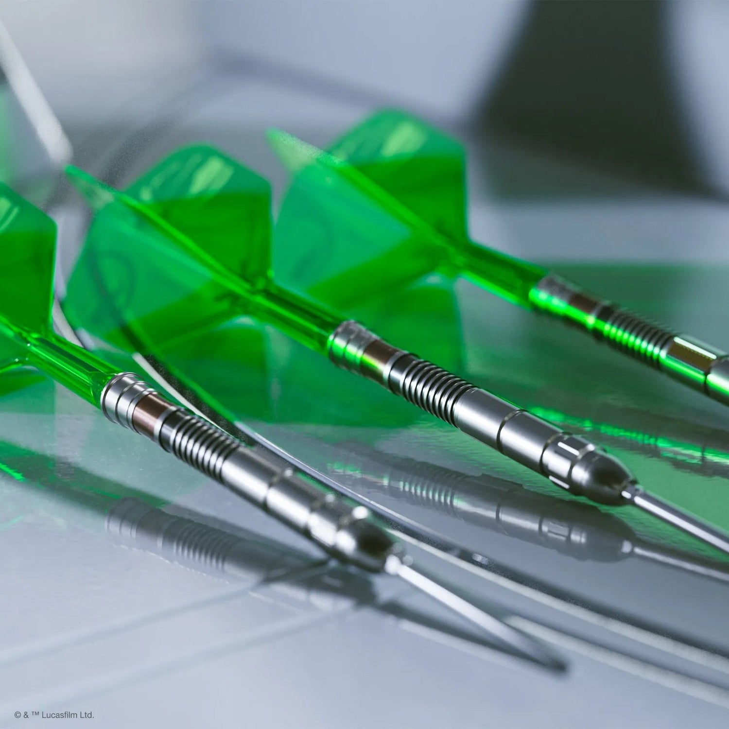 Angled close-up of three 95% tungsten darts with detailed grip barrels and green flights displayed on reflective surface