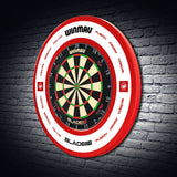 Red dartboard surround fitted around dartboard on brick wall, full view highlighting protective design for stray darts