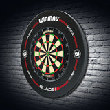 Angled shot of black dartboard surround and dartboard mounted on a brick wall, showing full protective ring and clear score zone details